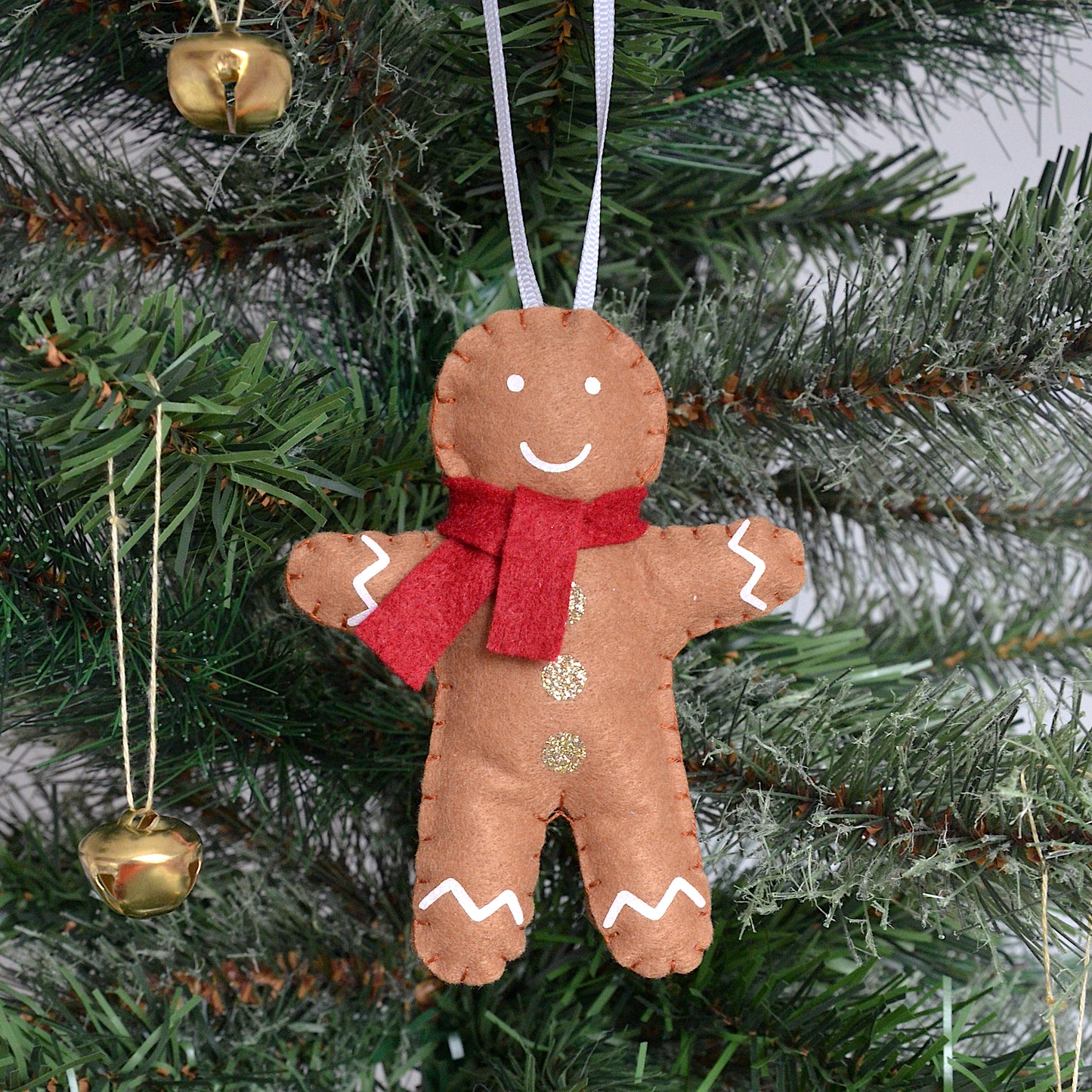 Gingerbread man ornament with a red scarf hanging on a Christmas tree.