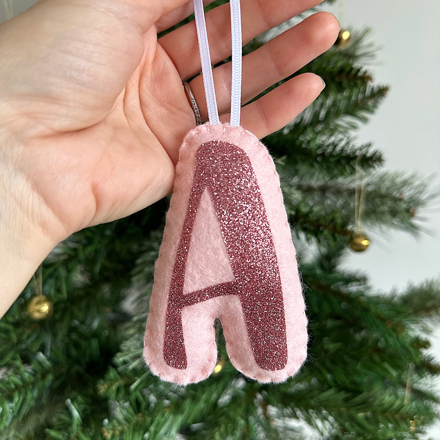 pink letter decoration held in front of a Christmas tree