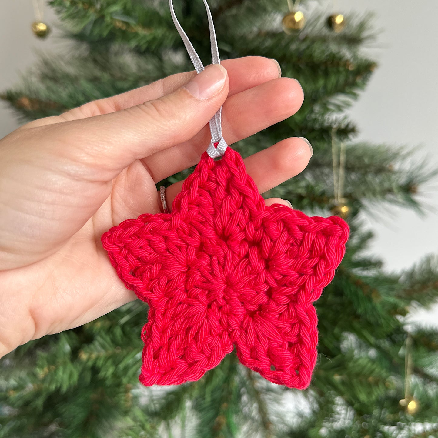 Red crocheted star ornament in front of a Christmas tree