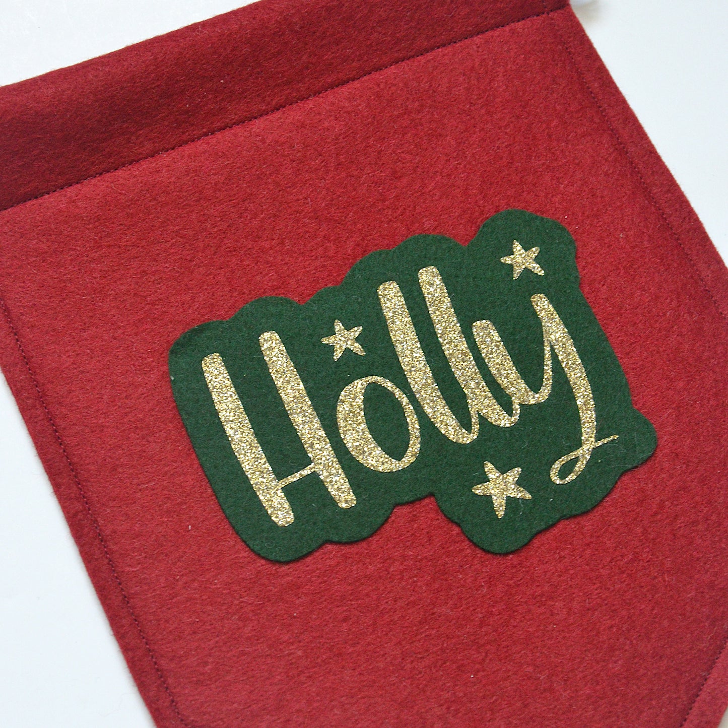 red felt banner in Christmas colours personalised with a name in gold glitter as well as gold star detail.