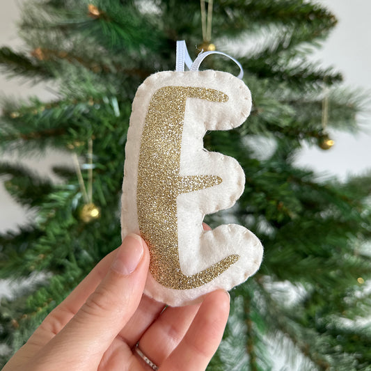Cream letter decoration with gold glitter detail in front of a Christmas tree