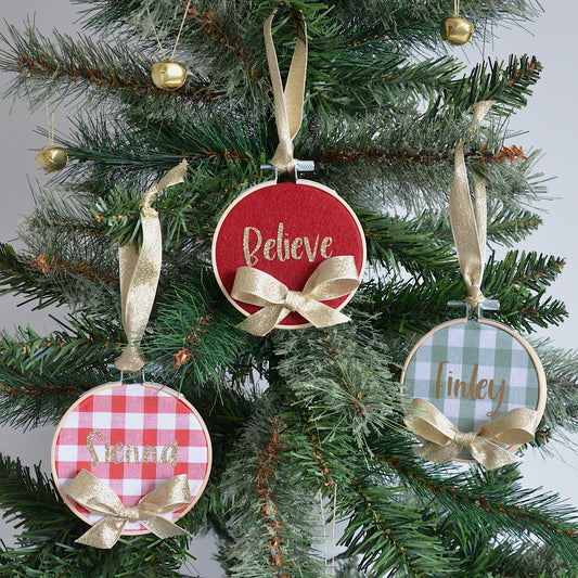 Decorative Christmas ornaments with names and festive phrases hanging on a tree.