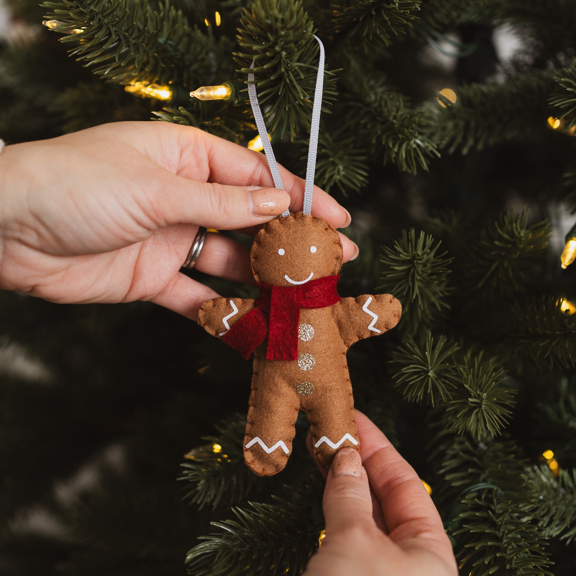 Gingerbread man ornament with a red scarf hanging on a Christmas tree.