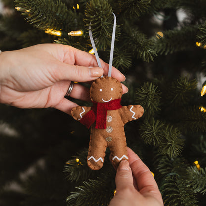 Gingerbread man ornament with a red scarf hanging on a Christmas tree.