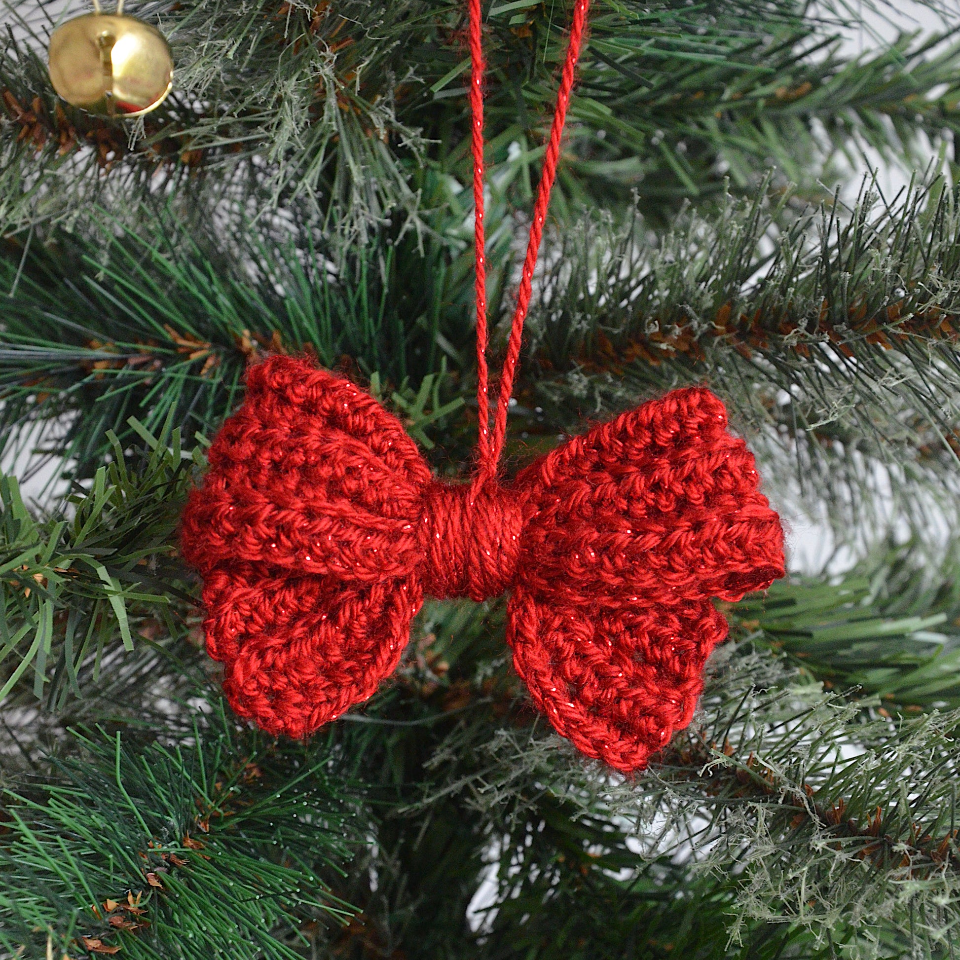 Red crocheted bow ornament hanging on a Christmas tree.