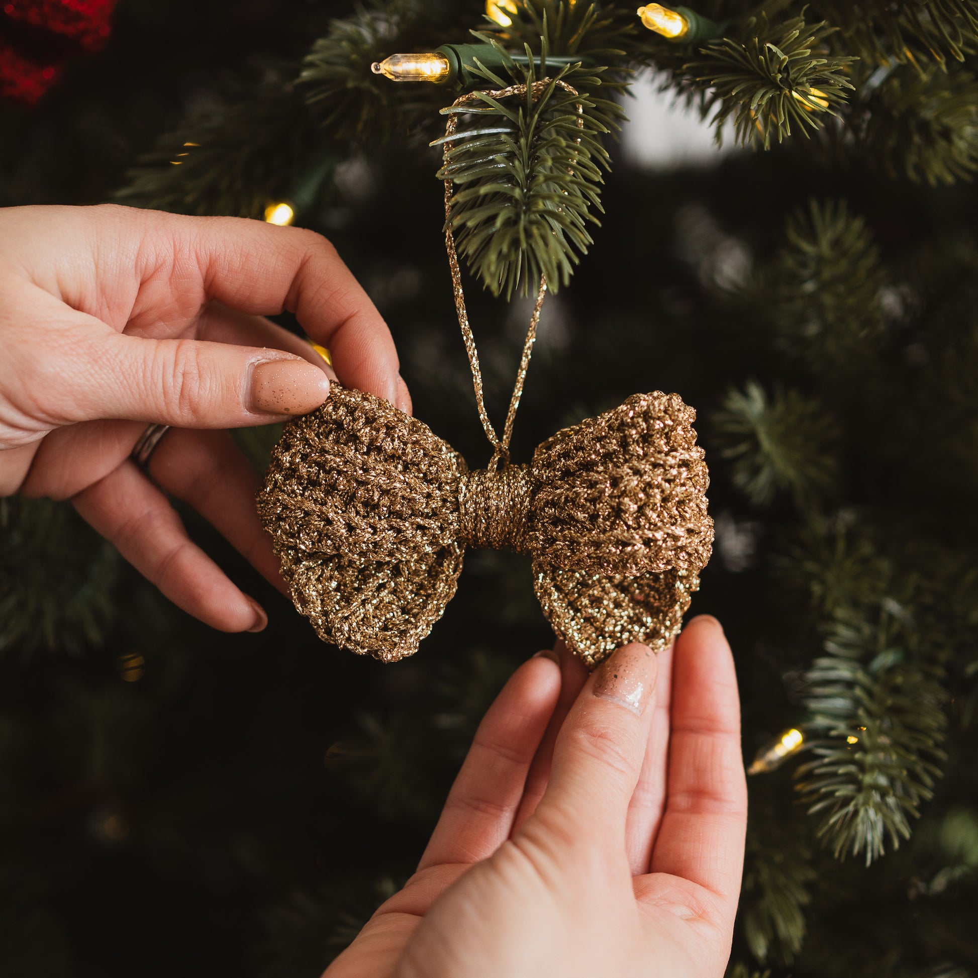Gold glittery bow decoration held in front of a Christmas tree