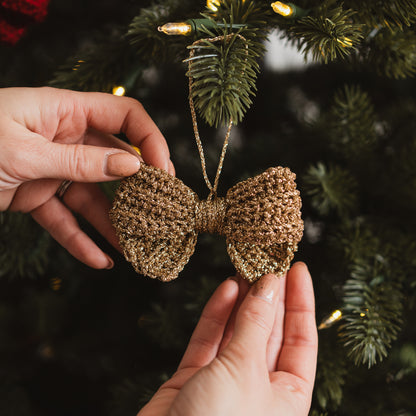 Gold glittery bow decoration held in front of a Christmas tree