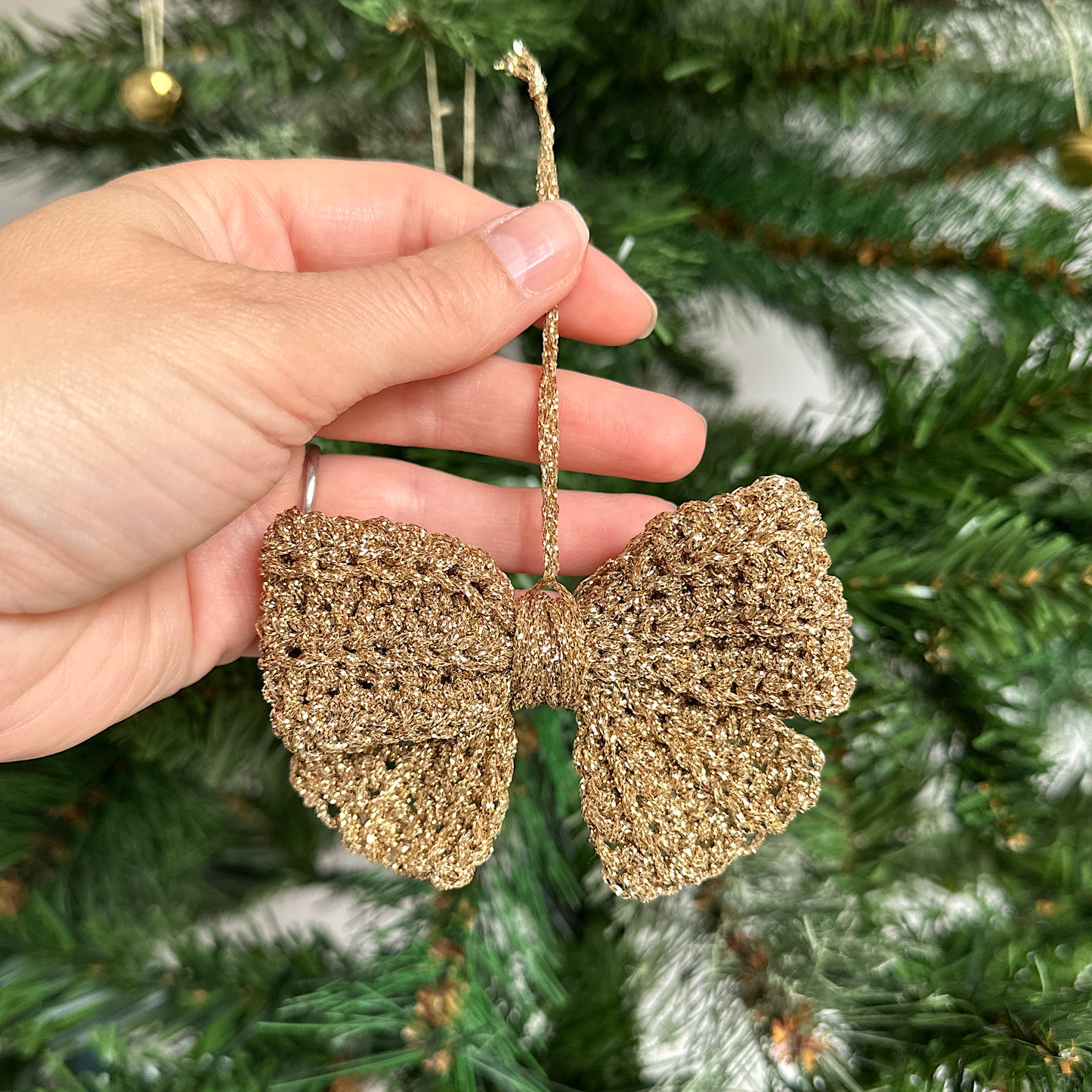 Gold glittery bow decoration held in front of a Christmas tree