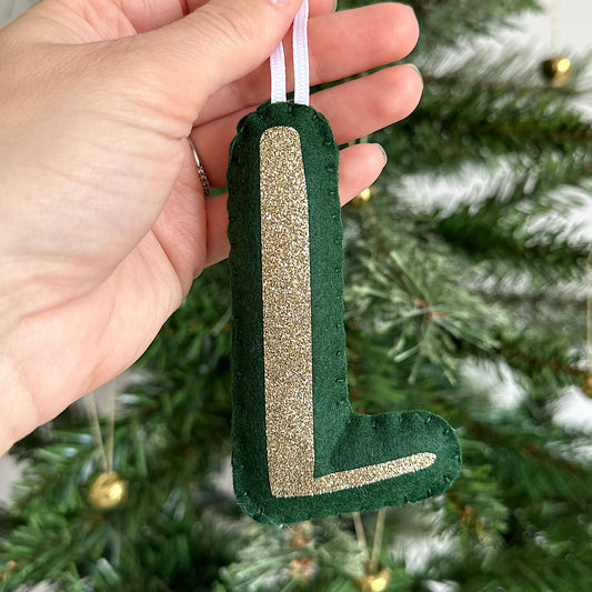 Green felt letter decoration with gold glitter held in front of a Christmas tree.