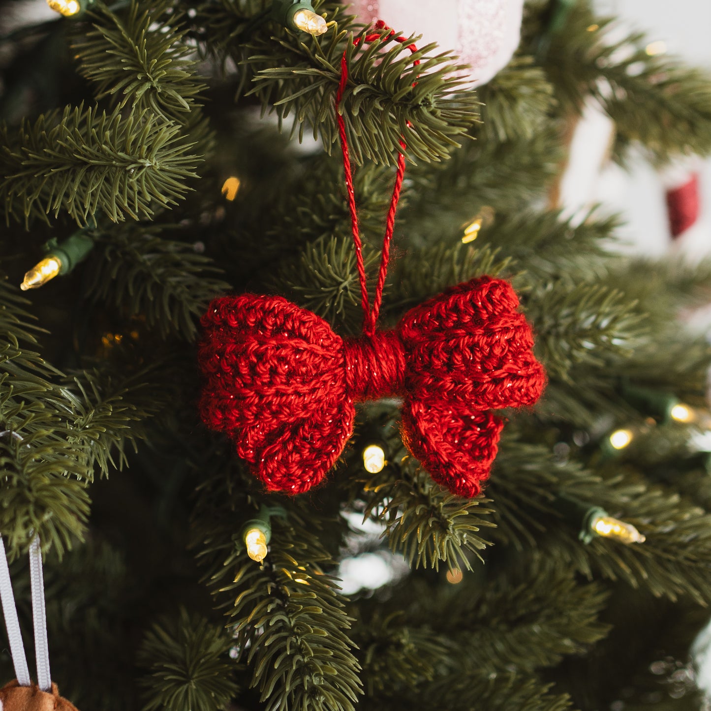 Red crocheted bow ornament hanging on a Christmas tree.