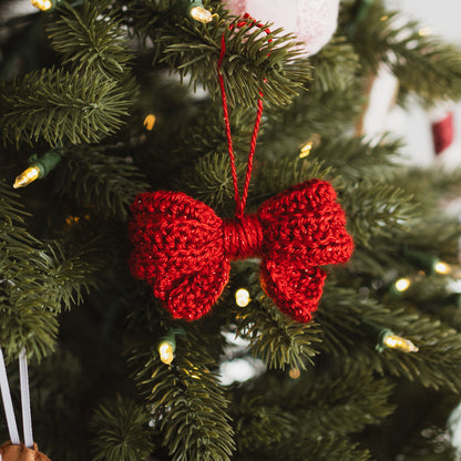 Red crocheted bow ornament hanging on a Christmas tree.