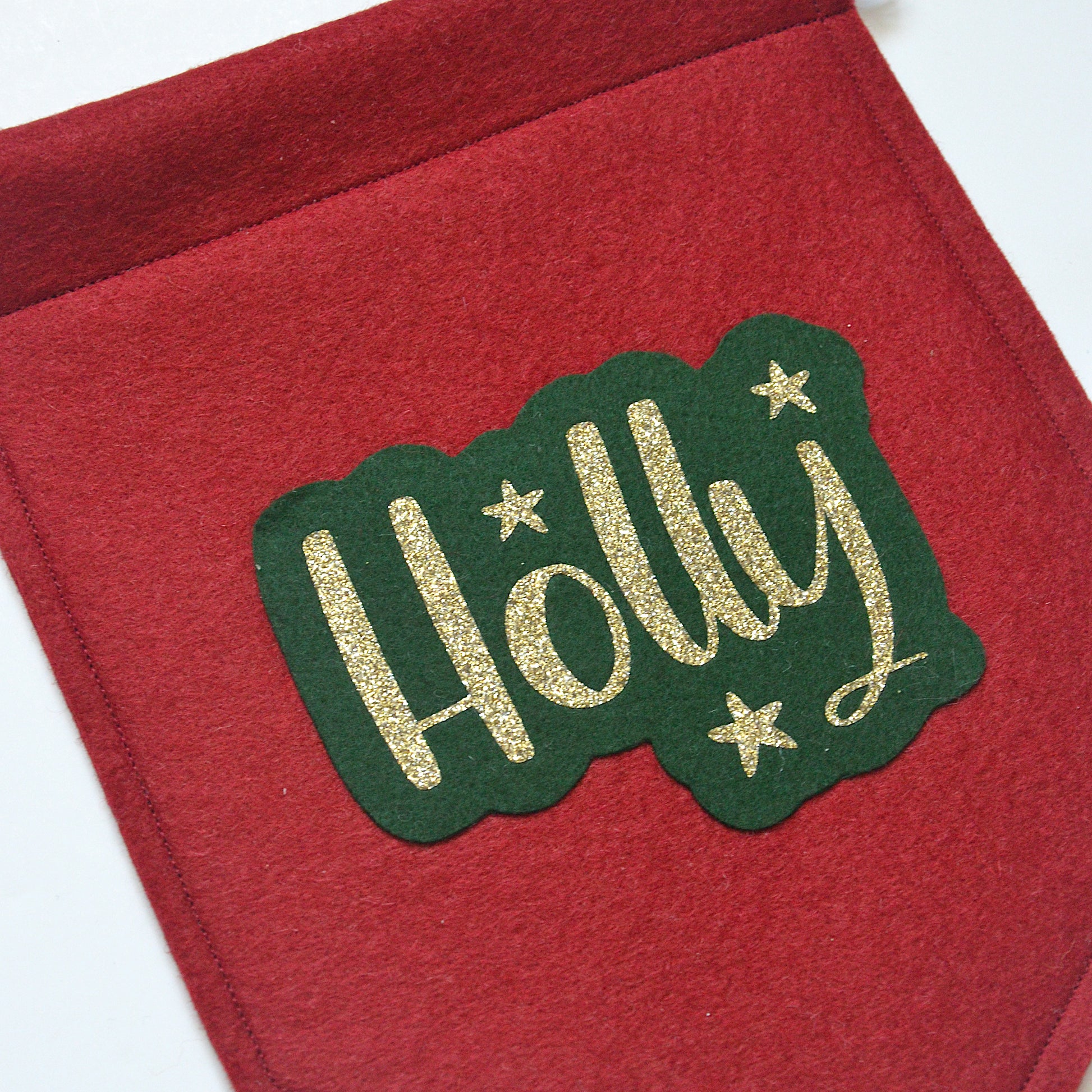 red felt banner in Christmas colours personalised with a name in gold glitter as well as gold star detail.